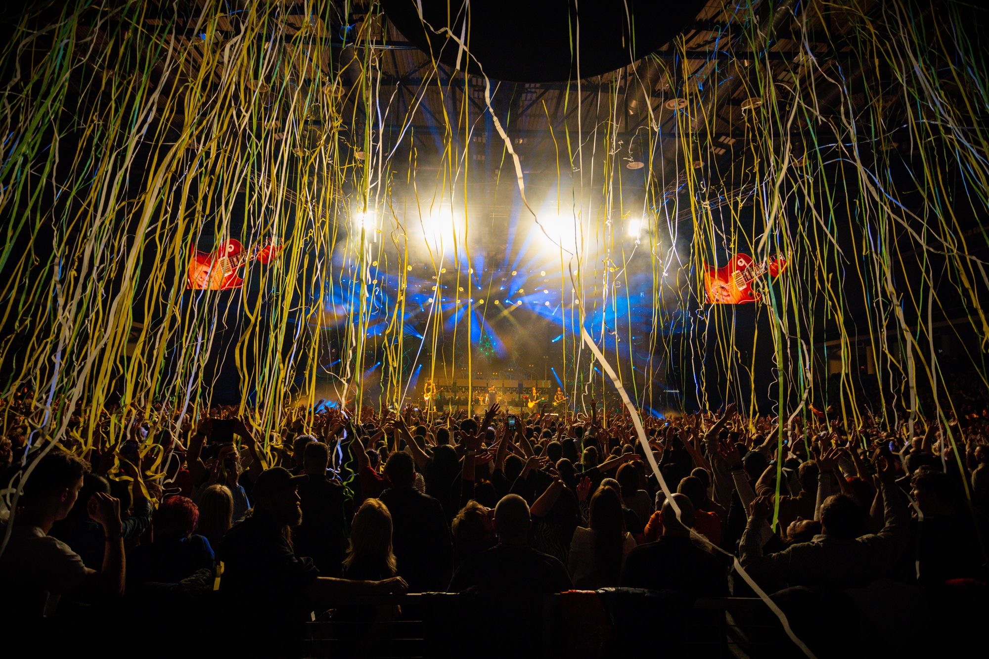 A festival crowd with hands in the air as confetti falls under the stage lights